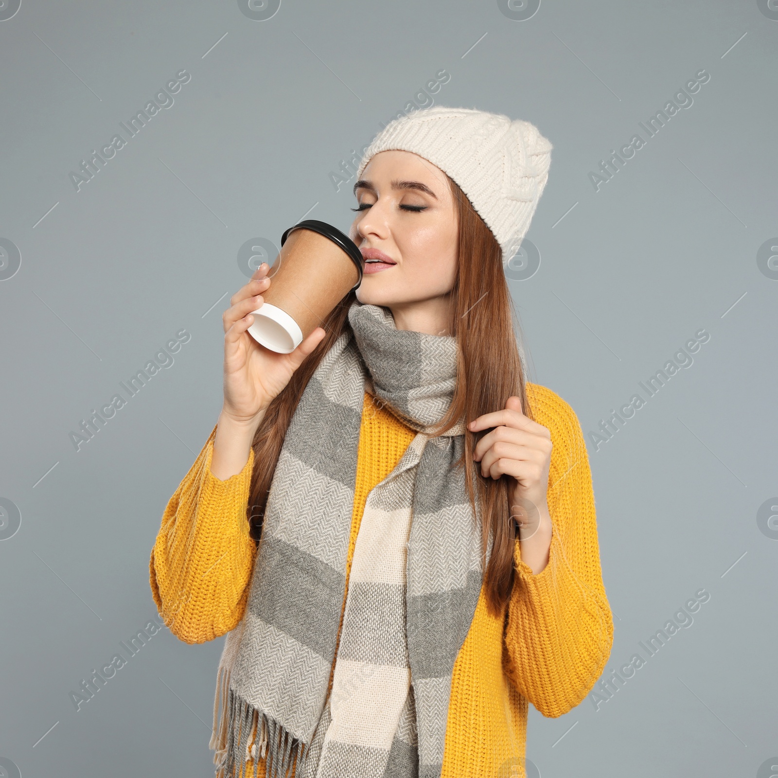 Photo of Happy young woman in warm clothes with drink on grey background. Winter season