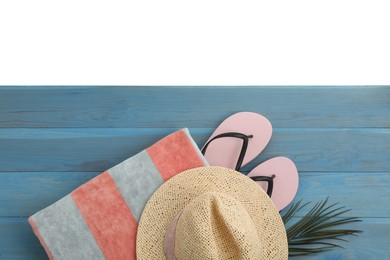 Light blue wooden surface with beach towel, straw hat and flip flops on white background, top view