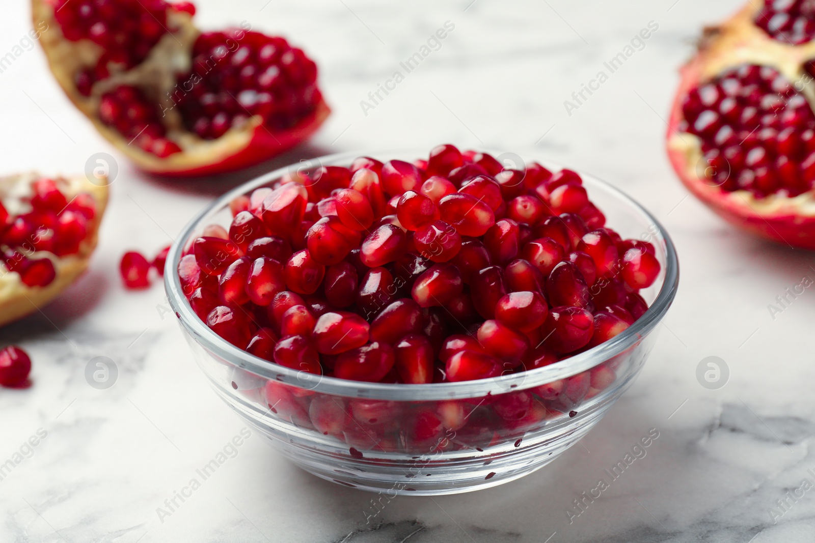 Photo of Ripe juicy pomegranate grains in bowl on white marble table