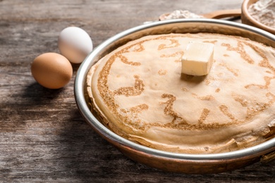 Photo of Frying pan with thin pancakes and butter on table