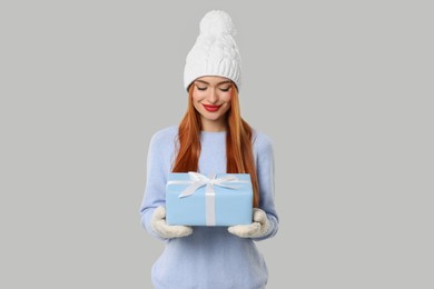 Young woman in hat and sweater with Christmas gift on light grey background