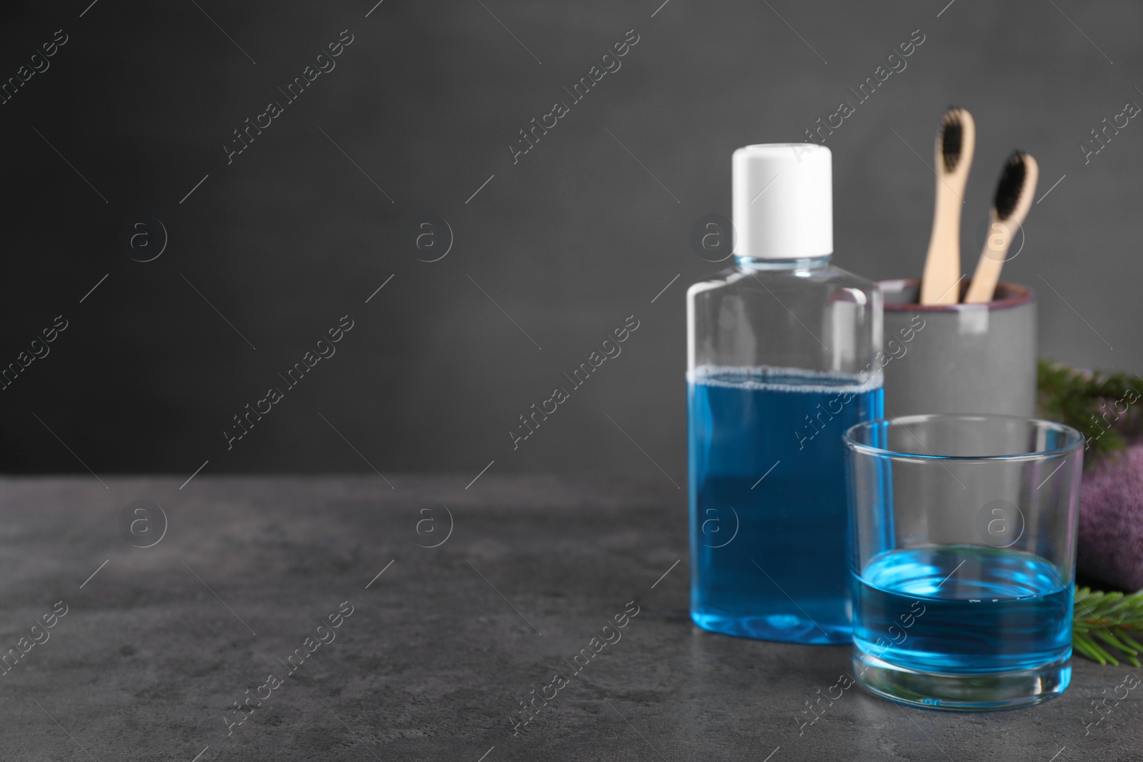 Photo of Fresh mouthwash in glass and bottle on dark textured table, closeup. Space for text