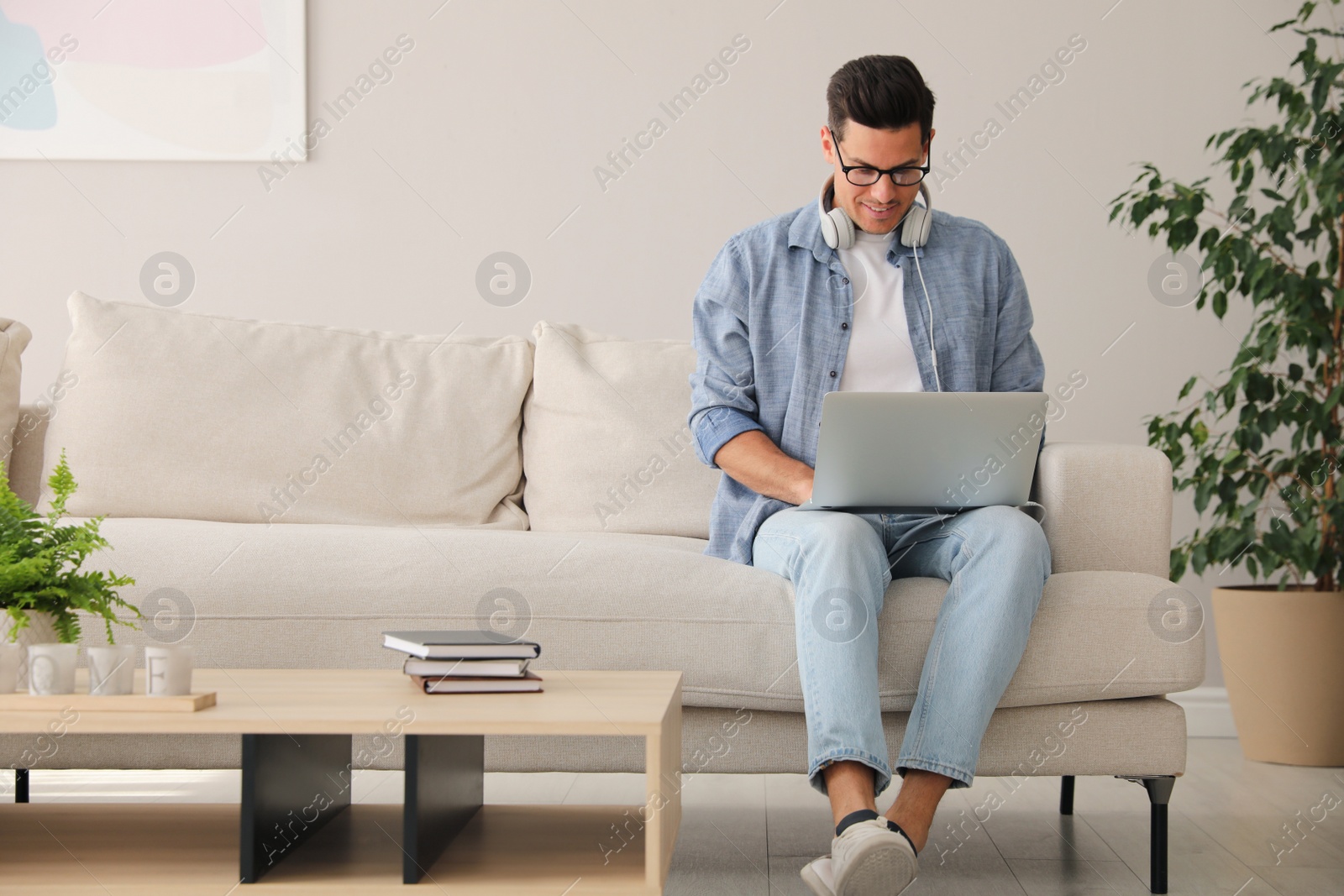 Photo of Man with laptop and headphones sitting on sofa at home