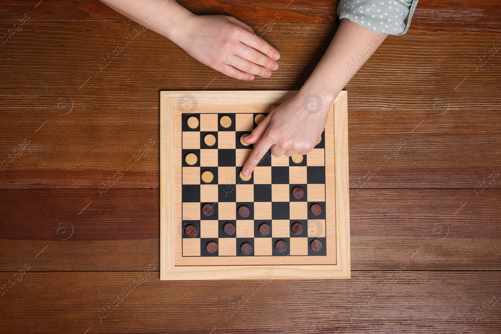 Photo of Playing checkers. Woman thinking about next move at wooden table, top view
