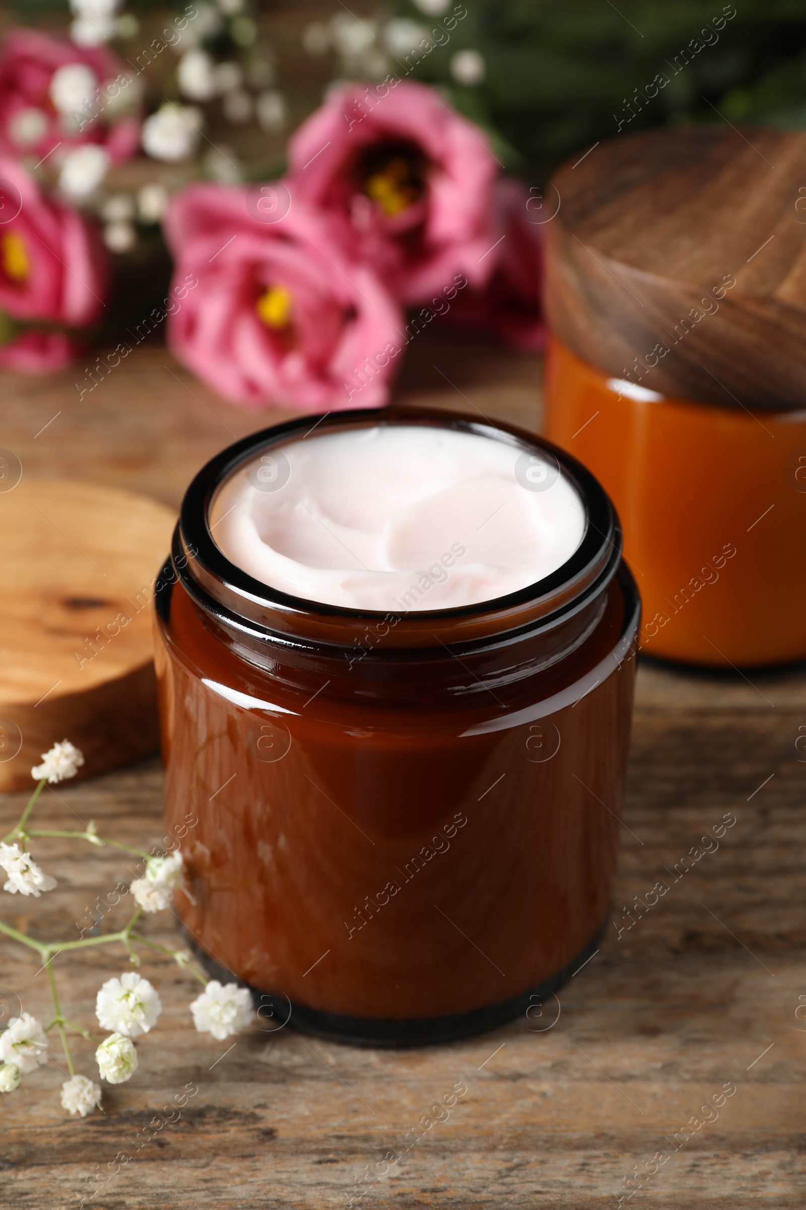 Photo of Jars of face cream and beautiful flowers on wooden table