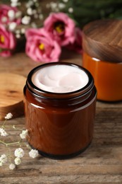 Photo of Jars of face cream and beautiful flowers on wooden table