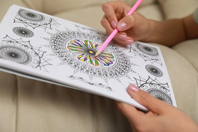 Photo of Young woman coloring antistress page near sofa, closeup