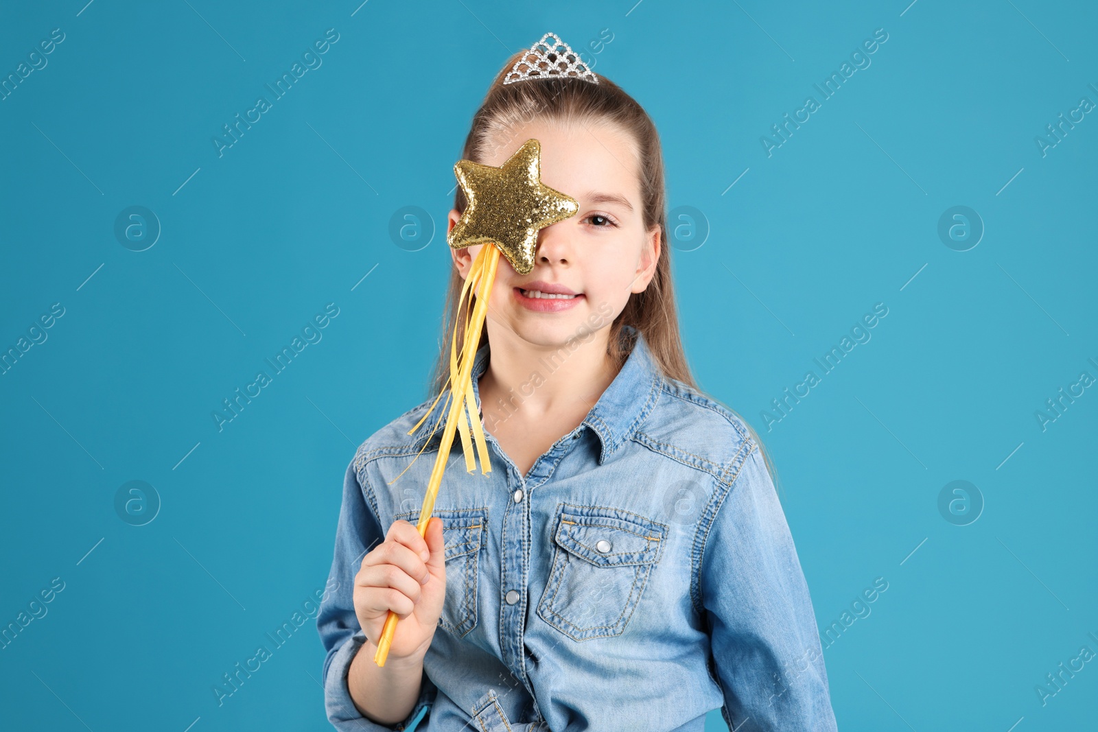 Photo of Cute girl in diadem with magic wand on light blue background. Little princess