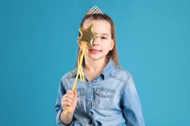 Photo of Cute girl in diadem with magic wand on light blue background. Little princess