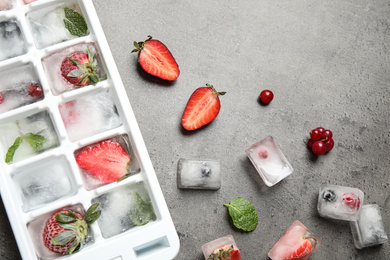 Photo of Ice cubes with berries and tray on grey table, flat lay