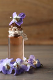 Photo of Beautiful wild violets and essential oil on wooden table. Spring flowers