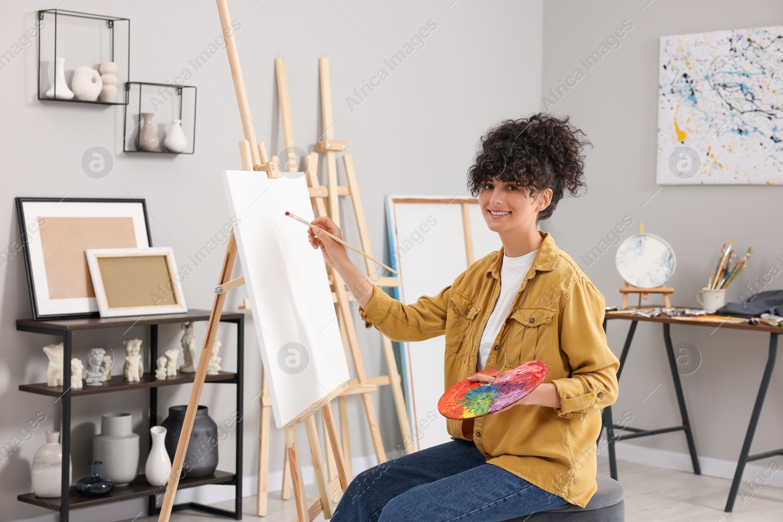 Photo of Young woman painting on easel with canvas in studio