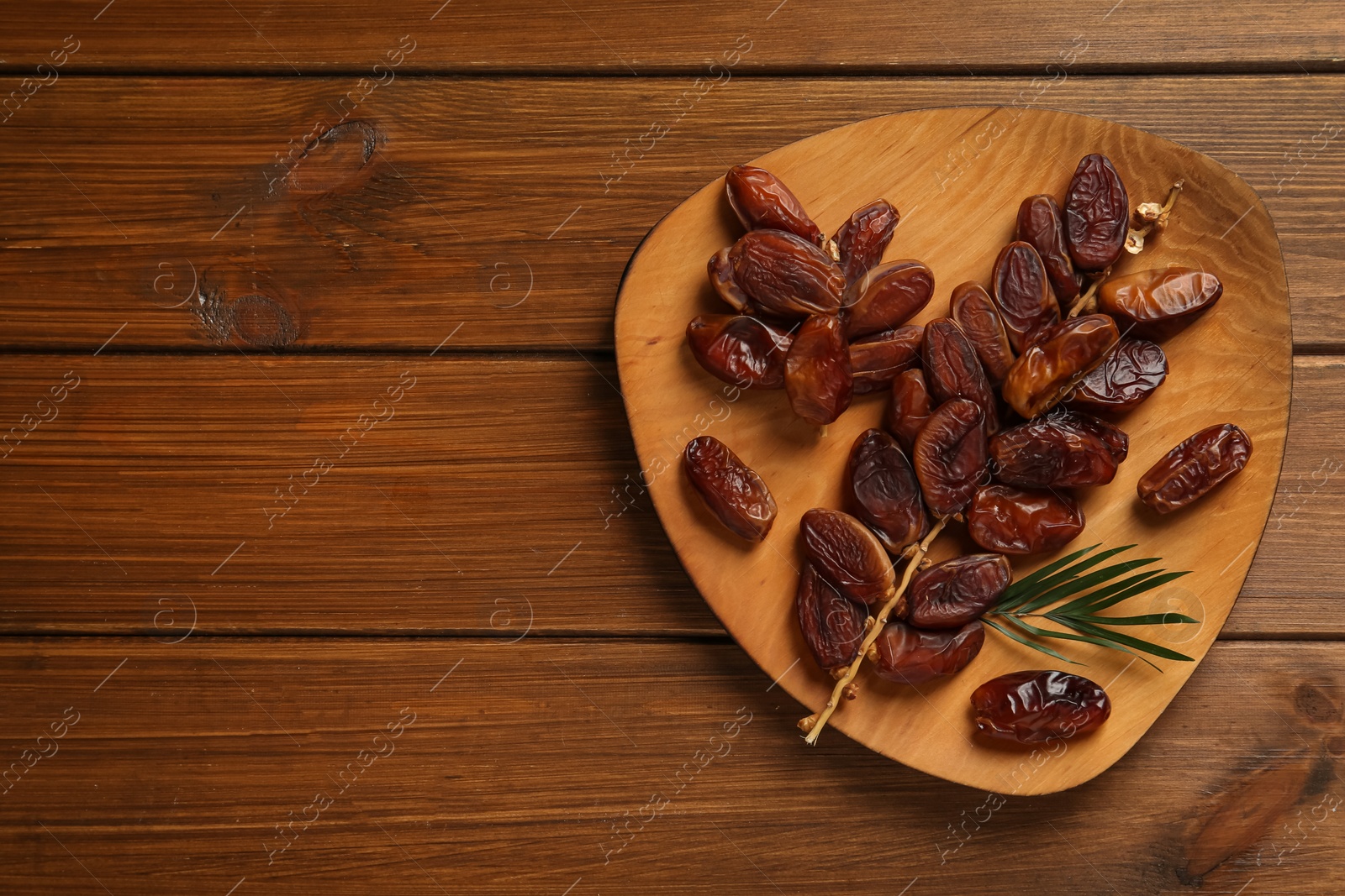 Photo of Branch with sweet dried dates and green leaf on wooden table, top view. Space for text