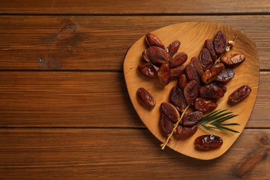 Branch with sweet dried dates and green leaf on wooden table, top view. Space for text