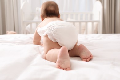 Photo of Little baby in diaper on bed at home, back view