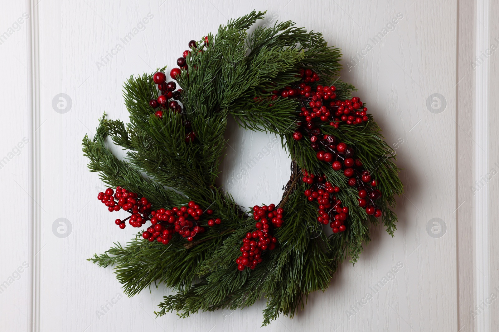 Photo of Beautiful Christmas wreath with red berries hanging on white door