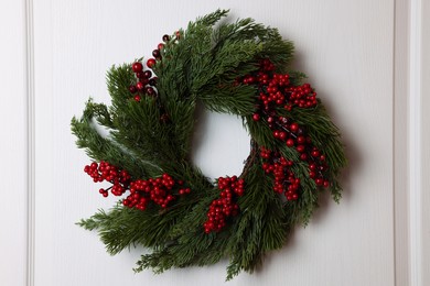 Beautiful Christmas wreath with red berries hanging on white door