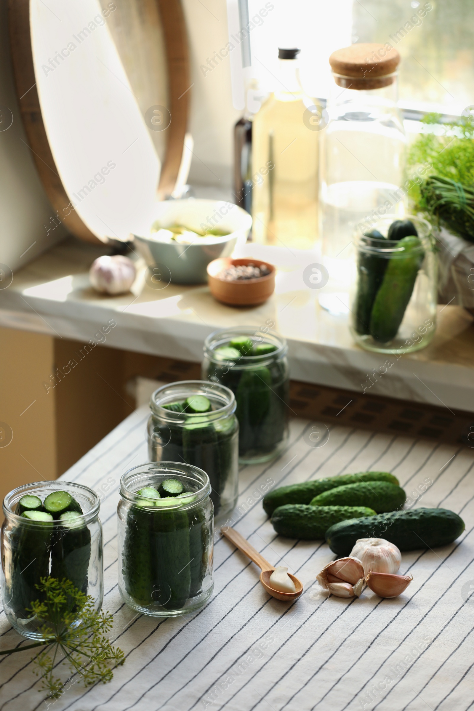 Photo of Glass jars with fresh cucumbers and other ingredients on table indoors. Canning vegetables