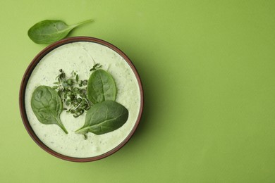 Delicious spinach cream soup with fresh leaves and microgreens in bowl on green background, top view. Space for text