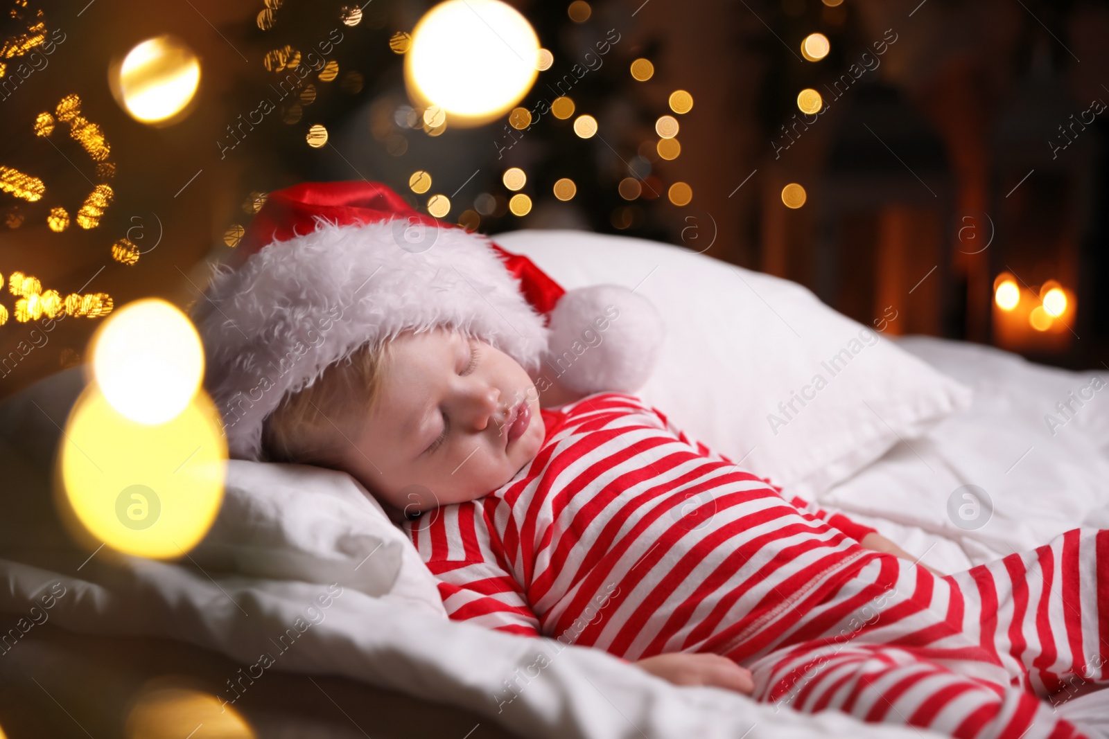 Photo of Baby in Christmas pajamas and Santa hat sleeping on bed indoors