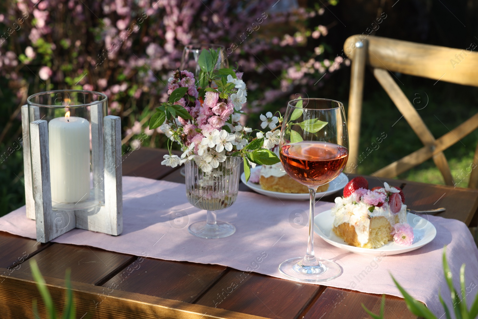 Photo of Vase with spring flowers, wine and cake on table served for romantic date in garden