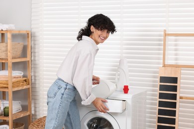 Woman pouring laundry detergent into washing machine indoors