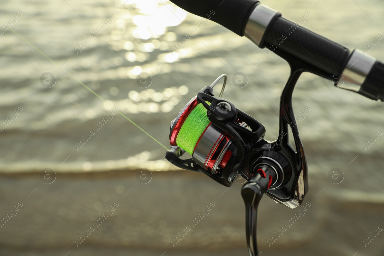 Photo of Fishing rod with reel near river, closeup. Space for text