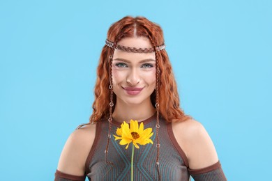 Beautiful young hippie woman with sunflower on light blue background