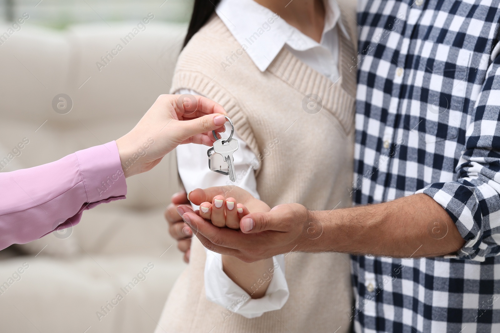 Photo of Real estate agent giving house key to couple indoors, closeup