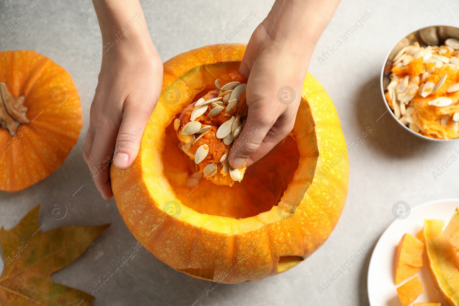 Photo of Woman making pumpkin head Jack lantern for Halloween at light table, top view