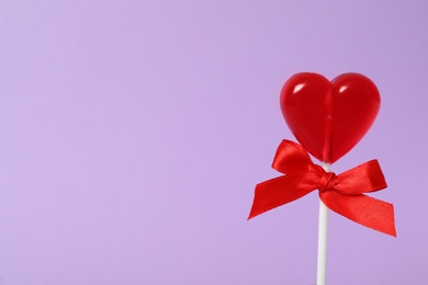 Photo of Sweet heart shaped lollipop on violet background, closeup view with space for text. Valentine's day celebration