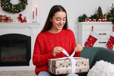 Photo of Happy young woman opening Christmas gift at home