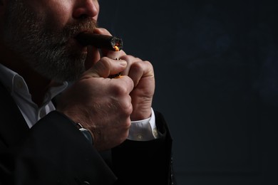 Photo of Bearded man lighting cigar on dark grey background, closeup. Space for text