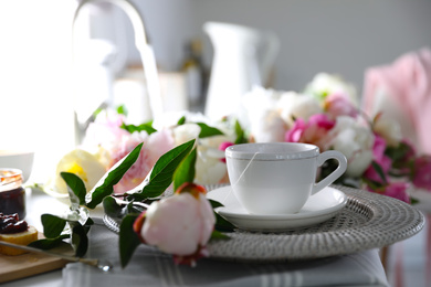 Beautiful peonies and cup of tea on table indoors