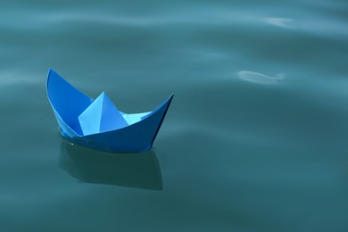 Photo of Light blue paper boat floating on water surface, space for text