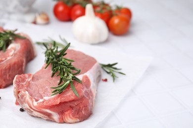 Photo of Fresh raw meat with rosemary on white tiled table, closeup. Space for text