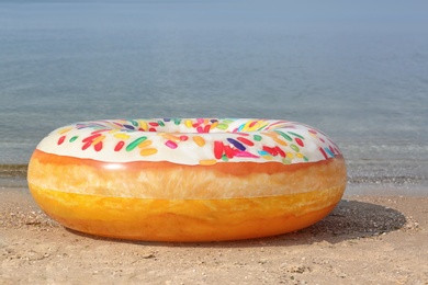 Photo of Bright inflatable doughnut ring near sea on sunny day