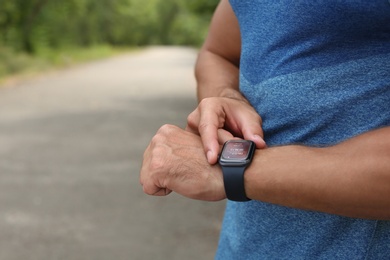 Man with smart watch checking time interval, distance, heart rate and burnt calories amount in fitness monitor app after training outdoors, closeup