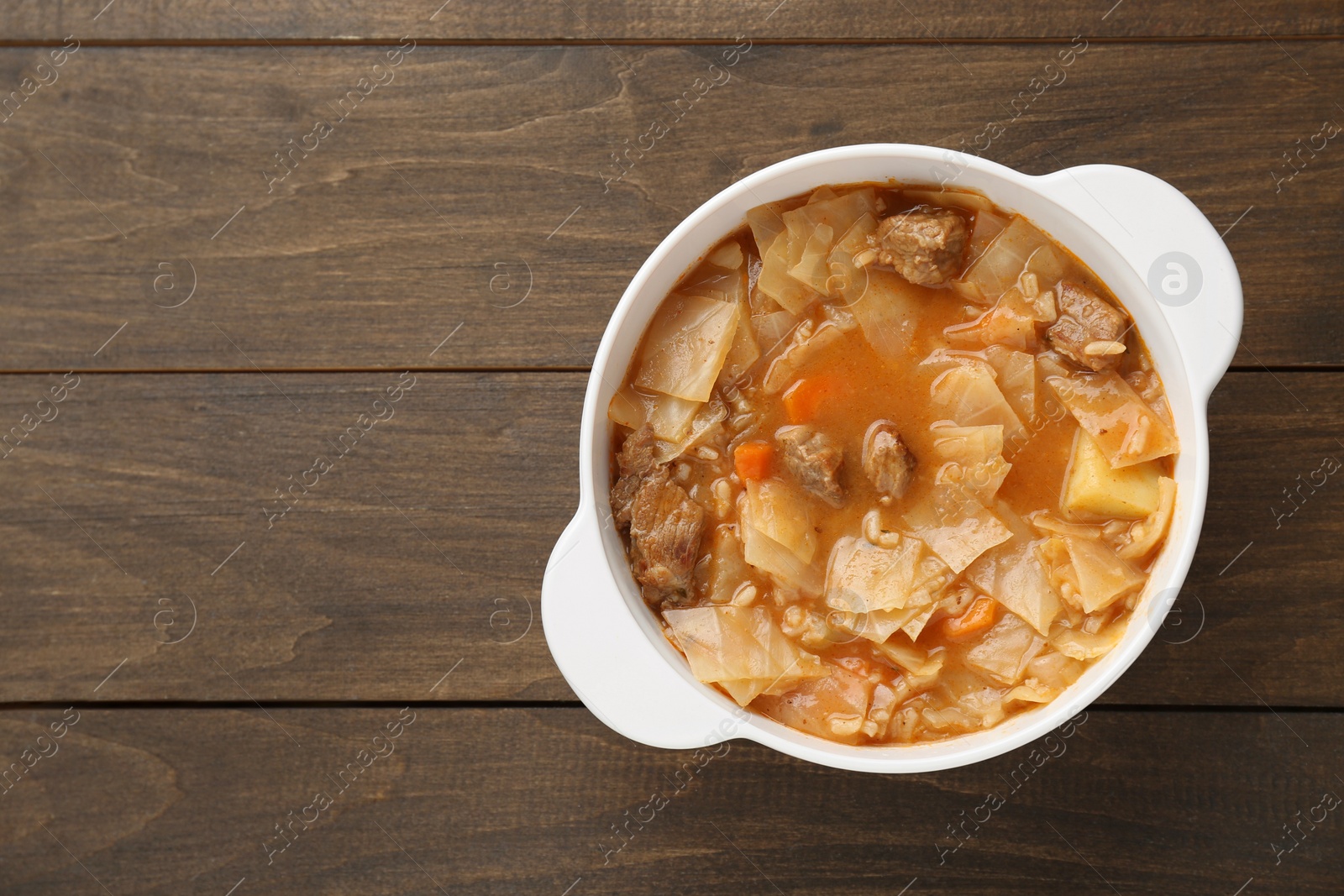 Photo of Tasty cabbage soup with meat and carrot on wooden table, top view. Space for text