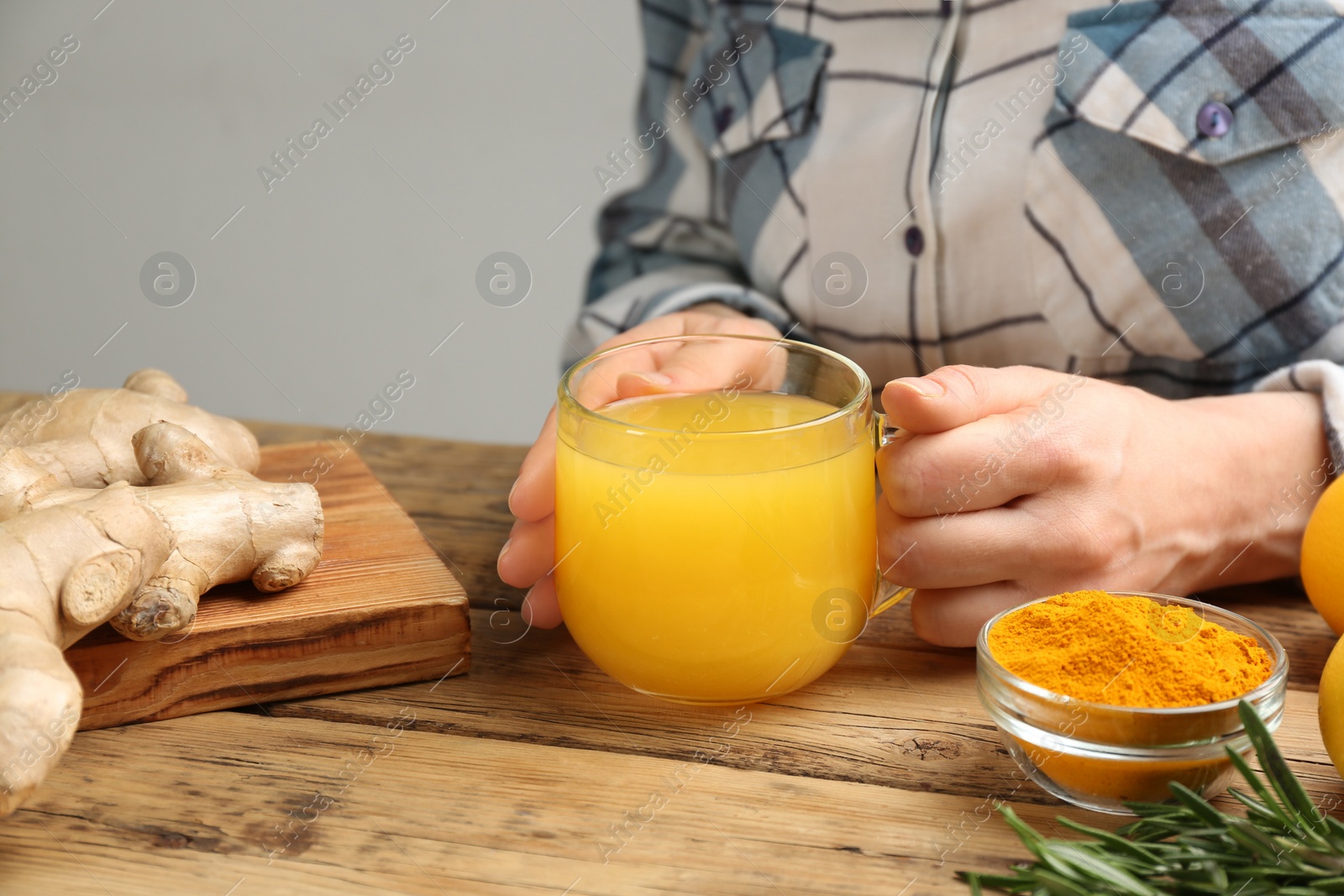 Photo of Woman holding cup of immunity boosting drink at wooden table with ingredients, closeup