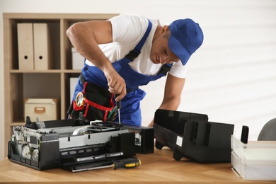 Repairman with screwdriver fixing modern printer in office