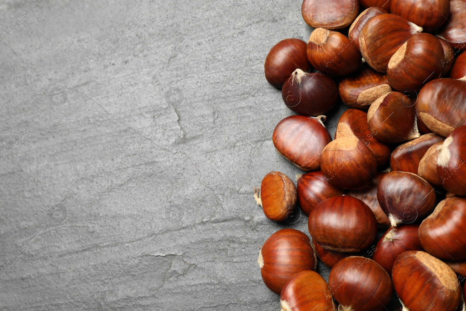 Photo of Fresh sweet edible chestnuts on black slate table, flat lay. Space for text