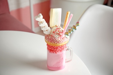 Photo of Tasty milk shake with sweets in mason jar on table at cafe