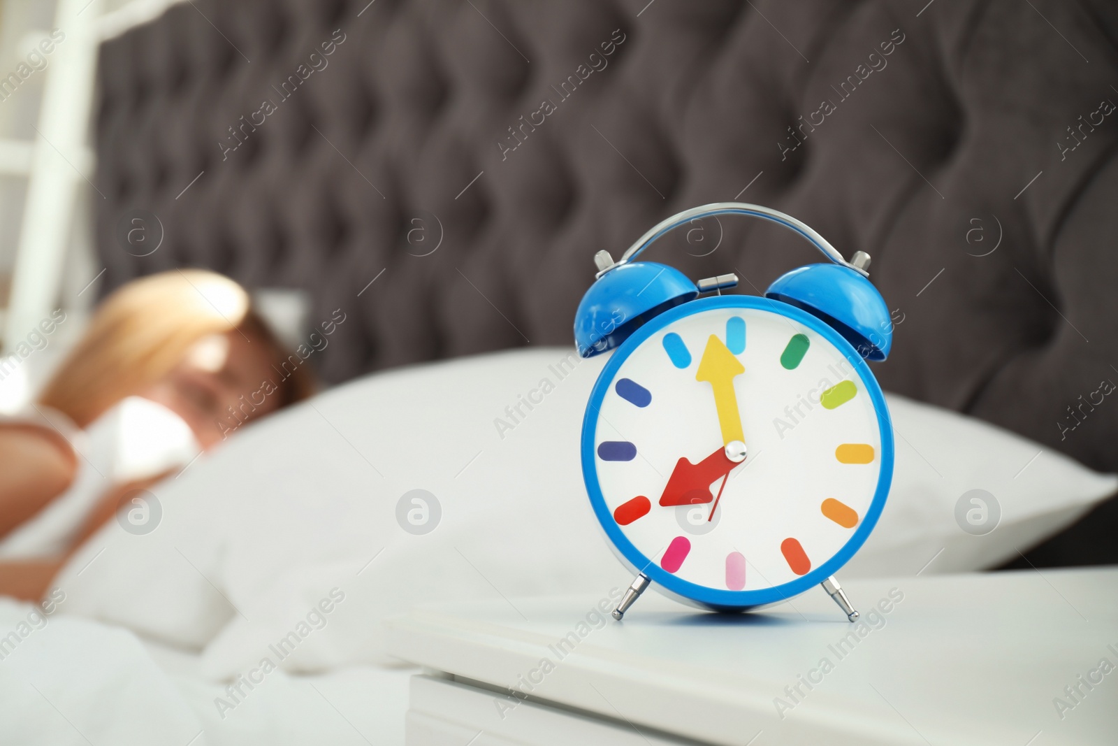 Photo of Analog alarm clock and blurred sleepy woman on background. Time of day