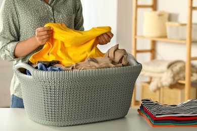 Photo of Woman with basket full of clean laundry at table indoors, closeup