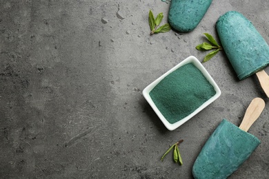 Flat lay composition with delicious spirulina popsicles and powder on grey background. Space for text