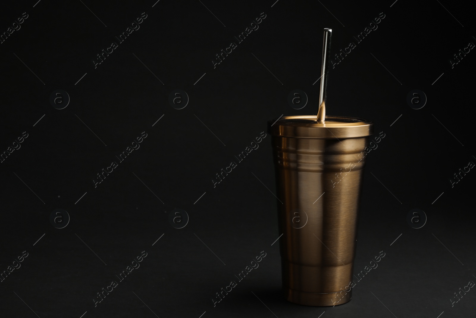 Photo of Gold cup with straw on black background. Space for text