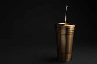 Gold cup with straw on black background. Space for text