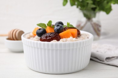 Photo of Delicious barley porridge with blueberries, pumpkin, dates and mint in bowl on white table, closeup