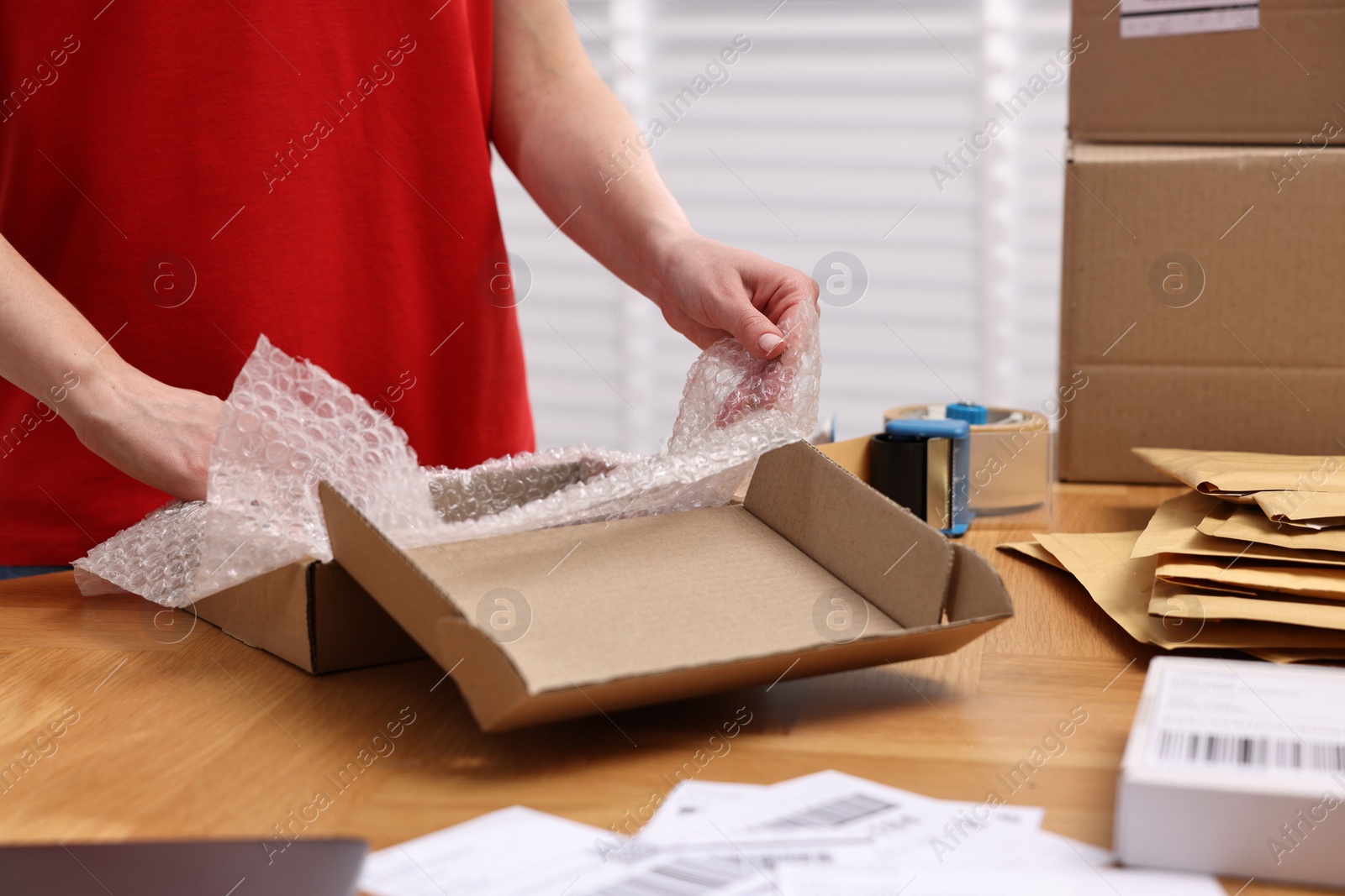 Photo of Post office worker packing parcel at wooden table indoors, closeup